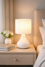 Load image into Gallery viewer, White ceramic lamp on a nightstand next to a bed with a headboard