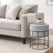Load image into Gallery viewer, Gray sofa with cushions and a small round ottoman in a living room setting.