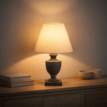 Load image into Gallery viewer, Table lamp on a wooden surface with a warm glow against a neutral wall.