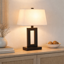 Load image into Gallery viewer, Table lamp with a white shade on a wooden surface with decorative items.