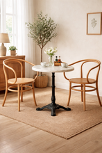 Load image into Gallery viewer, Round marble table with wooden chairs in a bright room with decor elements.