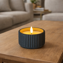 Load image into Gallery viewer, Candle in a ribbed container on a wooden table with a blurred living room background