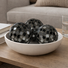 Load image into Gallery viewer, Decorative black spheres in a white bowl on a wooden table with a couch in the background