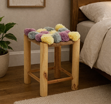 Load image into Gallery viewer, Wooden stool with colorful pom-pom cushion next to a bed in a bedroom setting.