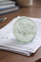 Load image into Gallery viewer, Green glass sphere with floral design on a stack of newspapers
