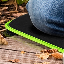 Load image into Gallery viewer, A close-up outdoor shot of a black cushioned pad with a bright neon green edge, partially covered by blue denim fabric, resting on a weathered wooden surface with dry leaves.