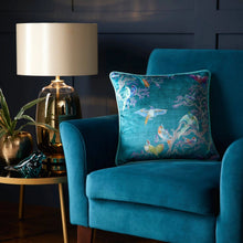 Load image into Gallery viewer, Blue armchair with a decorative pillow featuring birds and coral, next to a lamp and small table with decor items.
