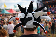 Load image into Gallery viewer, Person wearing a jester hat with red balls at a music festival.
