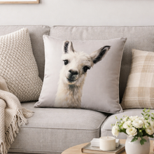 Load image into Gallery viewer, Gray sofa with a pillow featuring a llama face design, surrounded by decorative items.
