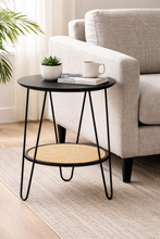 Load image into Gallery viewer, Small round side table with black metal legs and wooden shelf in a living room setting.
