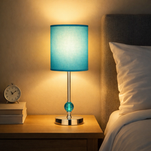 Load image into Gallery viewer, Blue lamp on a bedside table next to a bed with pillows

