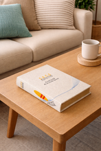 Load image into Gallery viewer, Book on a wooden coffee table with a cup in the background
