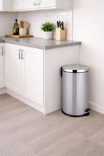 Load image into Gallery viewer, Silver trash can in a kitchen setting with white cabinets and a gray countertop.
