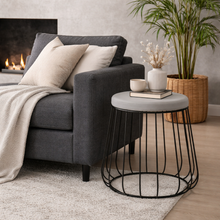 Load image into Gallery viewer, Living room with a gray sofa, round black wire side table, and decorative items.
