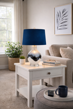 Load image into Gallery viewer, Living room with a side table featuring a blue lamp, books, and a mug.
