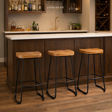 Load image into Gallery viewer, Three wooden bar stools with black metal legs in front of a bar setup.
