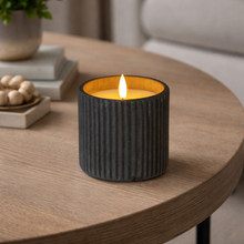 Load image into Gallery viewer, Candle in a textured black holder on a wooden table with a blurred background
