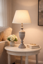 Load image into Gallery viewer, Table lamp on a round side table with a vase of flowers and a book in a cozy room setting.
