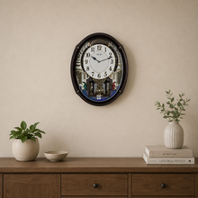 Load image into Gallery viewer, A round wall clock with a black frame and a printed cityscape face hangs on a beige wall above a wooden console table. The scene includes a potted plant, a small bowl, and a vase with branches on stacked books.

