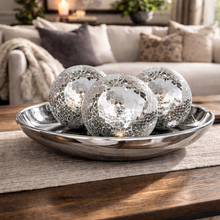 Load image into Gallery viewer, Decorative glass spheres in a metallic bowl on a wooden table with a cozy living room background.
