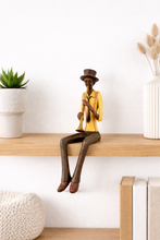 Load image into Gallery viewer, Statue of a person playing a instrument on a wooden shelf with decorative items.
