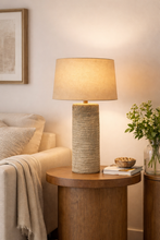 Load image into Gallery viewer, Lamp on a wooden side table with a cozy living room setting
