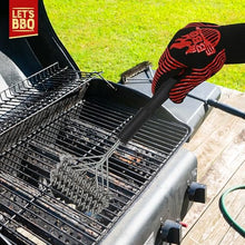 Load image into Gallery viewer, A red and black striped grill glove with a red flame logo is shown holding a long-handled metal grill scraper on a charcoal grill outdoors on a wooden deck with grass in the background.
